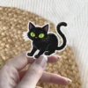 Illustration of a spooky black cat with large neon green eyes, vinyl sticker.