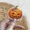 Carved Halloween pumpkin, glowing orange, filled with pink brain, lit candle, almonds, spooky smile, stitched detail vinyl sticker.