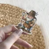 A charming illustrated sticker of a garden gnome with a white beard, holding a shovel and wearing a hat decorated with lavender.
