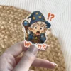 A shocked chibi wizard with a starry hat and staff exclaims 'Whattt?!' surrounded by punctuation marks, vinyl sticker.