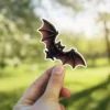 Chibi black bat, large golden yellow eyes, dark wings, whimsical halloween art, vinyl sticker.