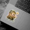 A cheerful blonde elf character in a green tunic and flower crown waves, with a bright sun icon and 'Good morning!' text, vinyl sticker.