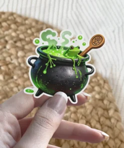 Cartoon frog in bubbling green potion, black cauldron, wooden spoon with pentagram, green drips, magical brew vinyl sticker.
