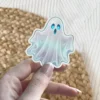 Small iridescent pastel ghost, glowing blue eyes, ethereal spooky aesthetic, die cut vinyl sticker.