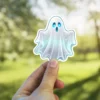 Glowing spectral phantom with wide blue eyes, ethereal white and teal highlights, vinyl sticker.