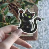 Waving black cat, vibrant green eyes, playful expression, artistic illustration, contour cut vinyl sticker