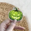 Vibrant green carved pumpkin, evil glowing yellow eyes, jagged mouth, intricate lightning cracks, vinyl sticker.