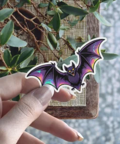 Cartoon purple bat, iridescent holographic wing details, sharp fangs, yellow eyes, gothic vinyl sticker.