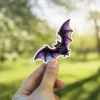 Holographic purple bat, iridescent wings, fanged creature, spooky nocturnal animal, stylized vinyl sticker.