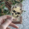Tan skull, dark horns, black recessed eye sockets, bold line art, vinyl sticker.