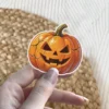 Orange cracked Jack-o'-lantern, triangular eyes, jagged smile, green stem, white border, vinyl sticker.