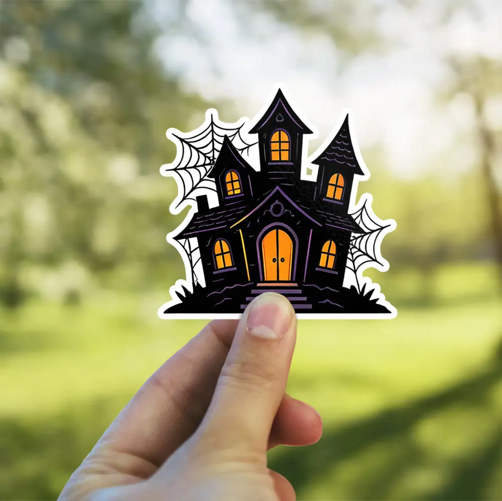 Spooky haunted house silhouette, glowing orange windows, intricate black spiderwebs, artistic gothic vinyl sticker.
