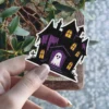 Haunted house silhouette, glowing yellow windows, white ghost doorway, purple accents, vinyl sticker.
