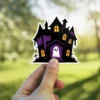 Haunted mansion, gothic architecture, glowing orange windows, friendly white ghost, purple accents, vinyl sticker