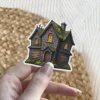 Haunted house, stone architecture, mossy roof, boarded windows, glowing orange light, vinyl sticker.
