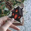 Haunted house, glowing windows, spider webs, bat silhouette, graveyard, dark gothic illustration, vinyl sticker.