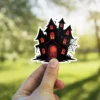 Haunted house silhouette, glowing red windows, spider webs, gothic mansion architecture, vinyl sticker