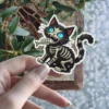 Black cat, skeleton ribs, glowing blue eyes, chomping fish bone, cartoon horror, vinyl sticker