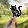 Black cat, skeleton ribs, spiderweb collar, vibrant green eyes, gothic Halloween illustration, vinyl sticker