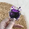 Detailed black cauldron holds vibrant purple bubbling potion, complete with a stirring stick and a crisp white outline vinyl sticker.