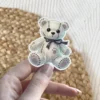Gothic teddy bear, stitched pattern, black bow, soft pastel aesthetic, cute creepy vinyl sticker.