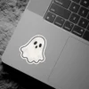 Playful light cream ghost shape, textured surface, black oval eyes, small mouth, distinct black outline, white kiss-cut border vinyl sticker.