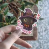 A winking black cat wearing a witch hat and cape, with the words 'Too cuteee' and hearts, as a vinyl sticker.